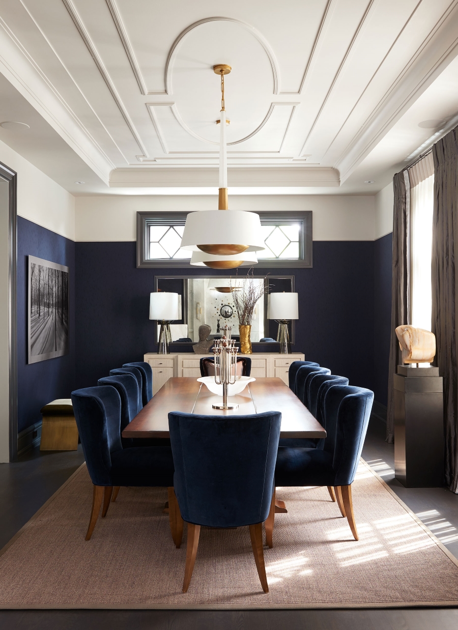Dining And Living Room Inspirations By Elizabeth Metcalfe. This modern-contemporary dining room has blue walls, a white console, white suspencion chandeliers,a wood dining table and dark blue armchairs.