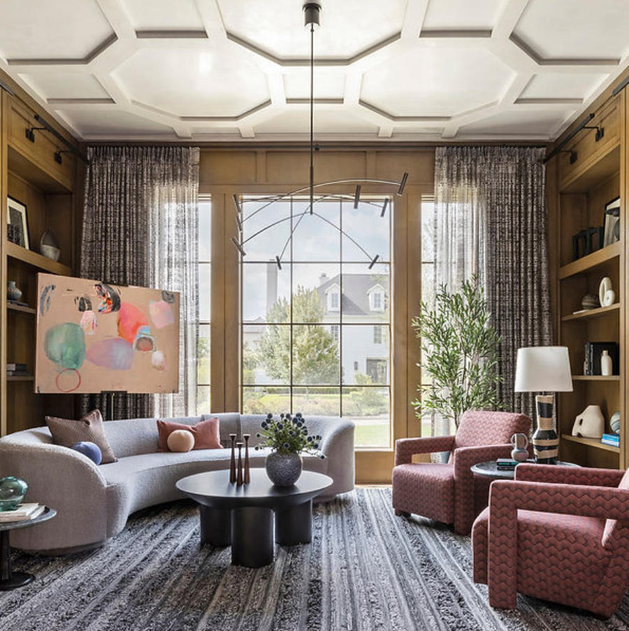 Benjamin Johnston Design: Dining And Living Room Inspiration. This living room has a grey sofa, two armchairs in red tones with a pattern, and a center table. There's a wide rug covering all the area.